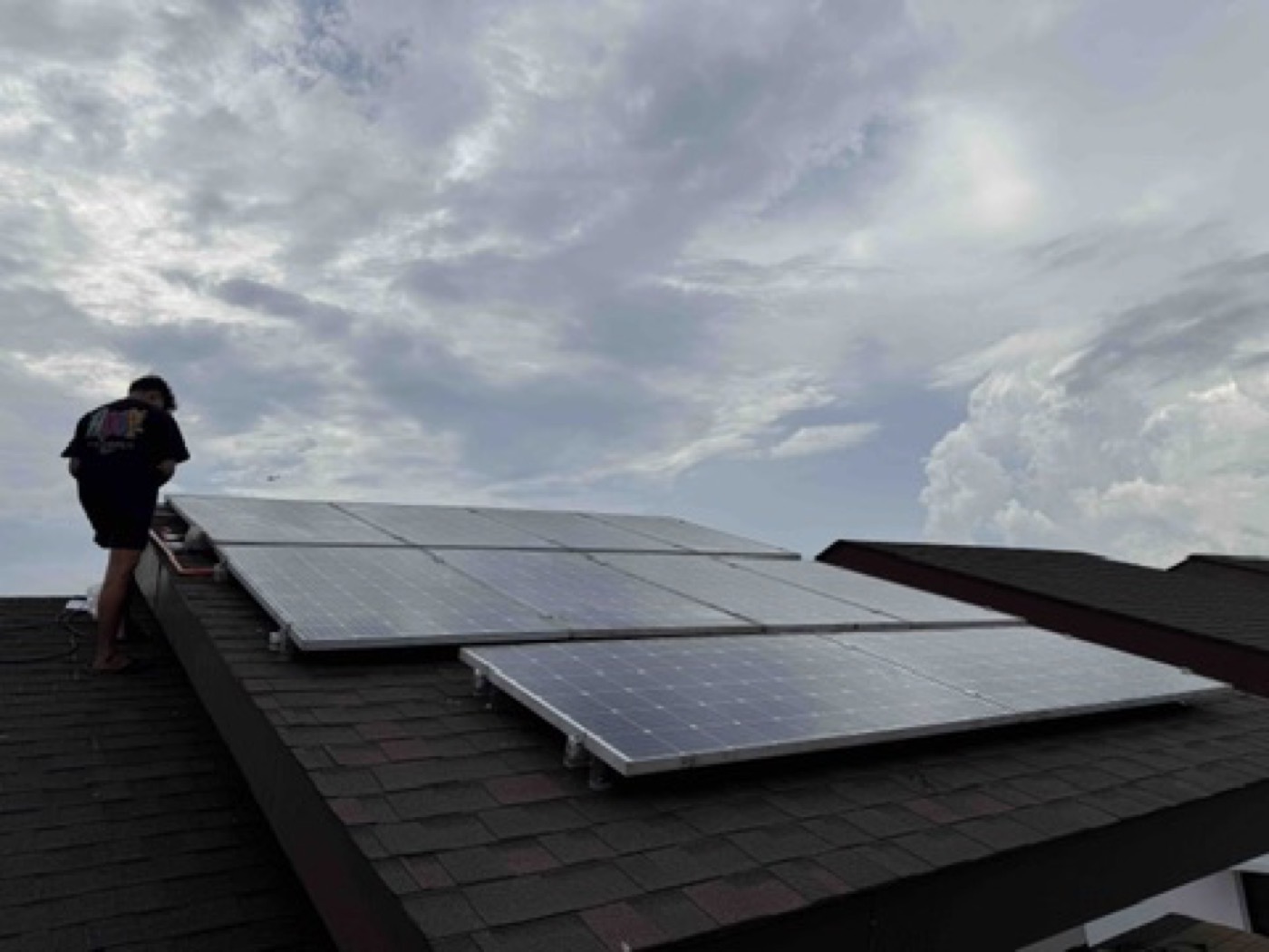 Residential rooftop solar array on a dark metal roof under a bright sky