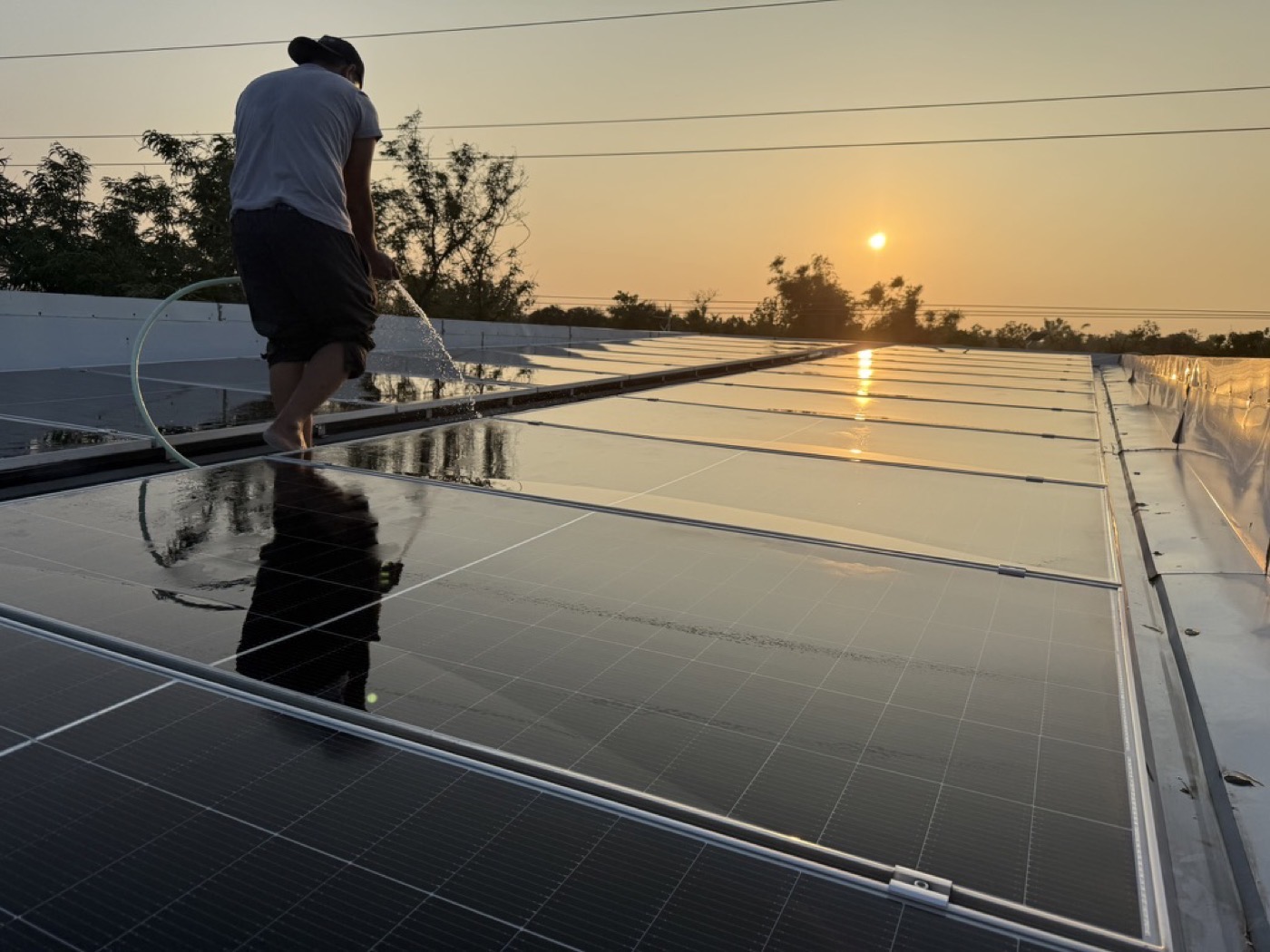 Rooftop solar array at sunset with an installer silhouetted against the sky